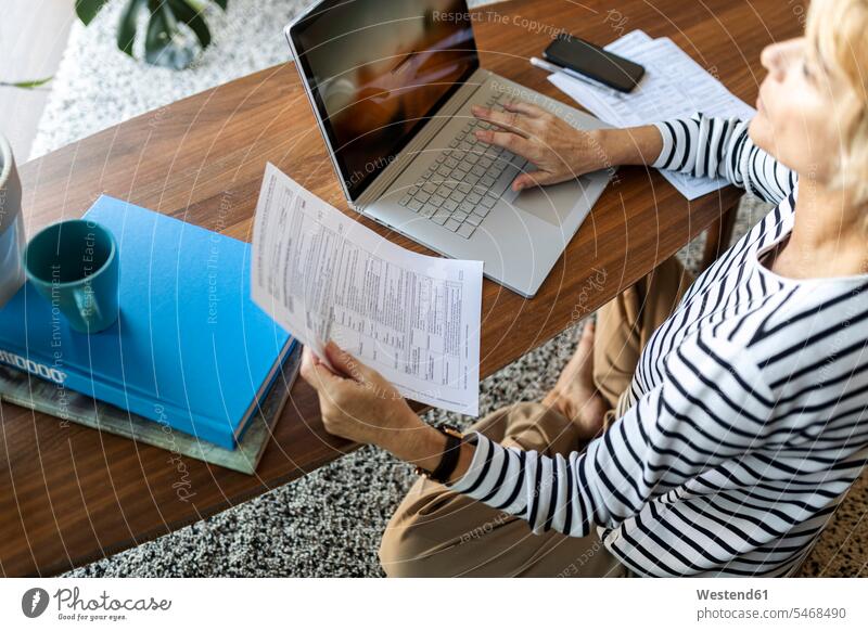 Mature woman with documents using laptop at home human human being human beings humans person persons celibate celibates singles solitary people solitary person