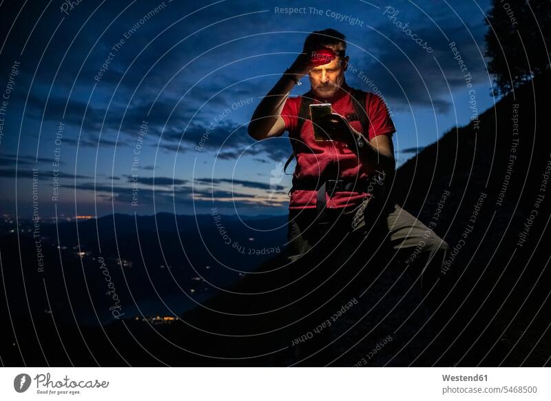Male hiker checking map over smart phone while standing on mountain at night, Orobie, Lecco, Italy color image colour image Orobie Mountains mountain range
