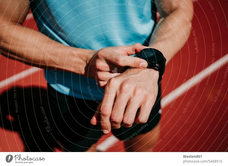 Male athlete on tartan track checking smartwatch watches wrist watches Wristwatch Wristwatches colour colours stand sports athletic sports track and field