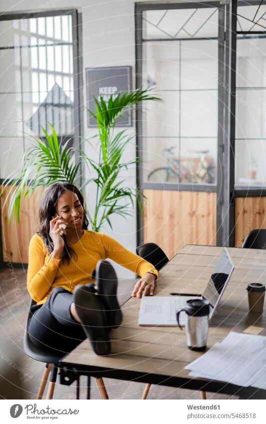 Young businesswoman sitting with feet on desk talking on cell phone desks on the phone call telephoning On The Telephone calling businesswomen business woman