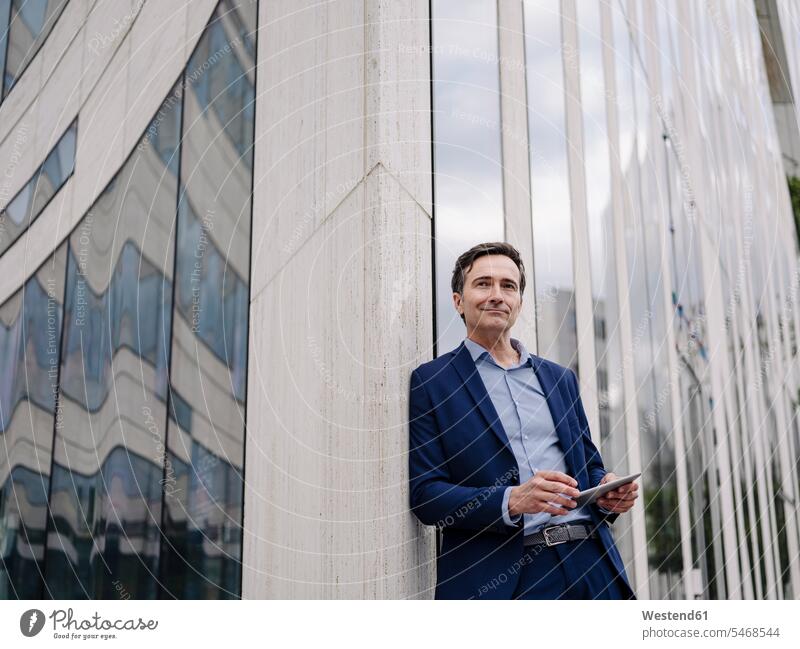Mature businessman with tablet leaning against a building in the city human human being human beings humans person persons caucasian appearance