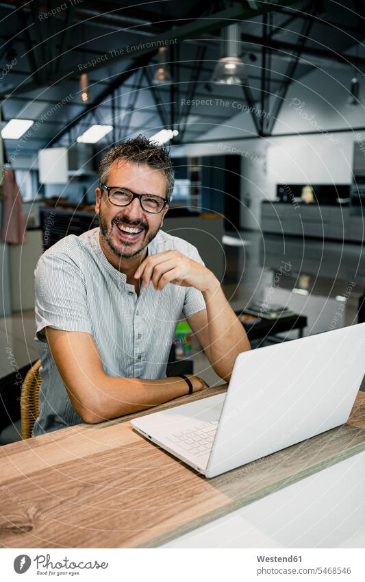 Cheerful handsome male freelancer sitting with laptop at desk while working in office color image colour image Spain indoors indoor shot indoor shots interior
