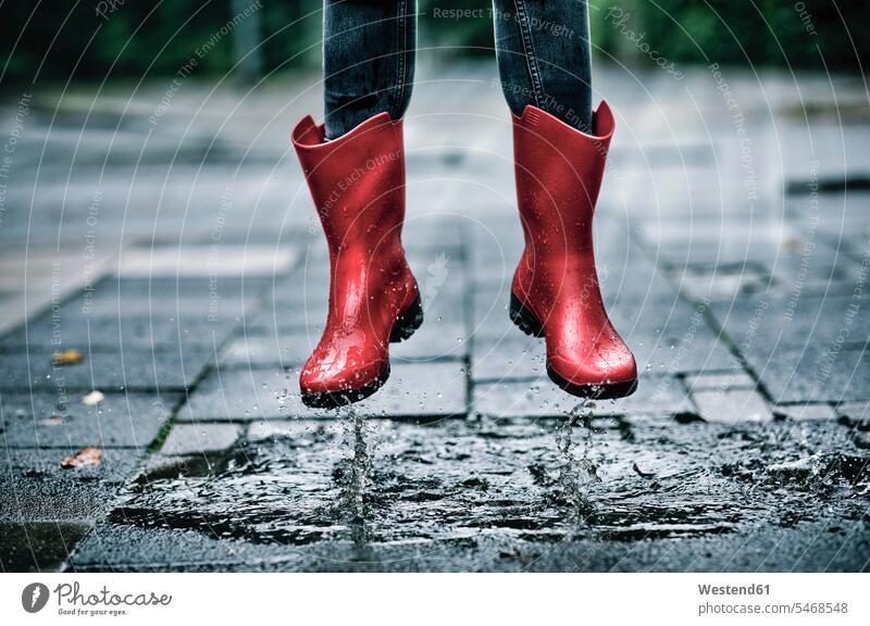 Feet of little girl wearing rubber boots jumping over small puddle outdoors location shots outdoor shot outdoor shots day daylight shot daylight shots day shots