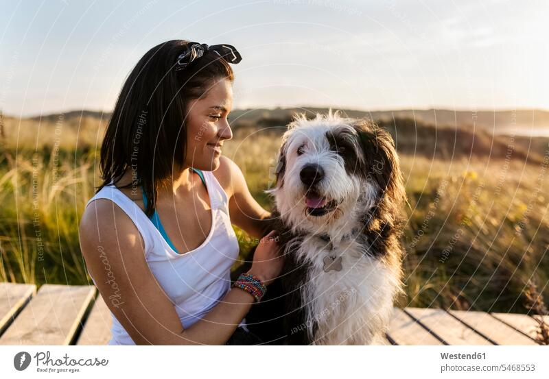 Smiling woman with dog on boardwalk in dunes animals creature creatures pet Canine dogs relax relaxing smile Seated sit embrace Embracement hug hugging