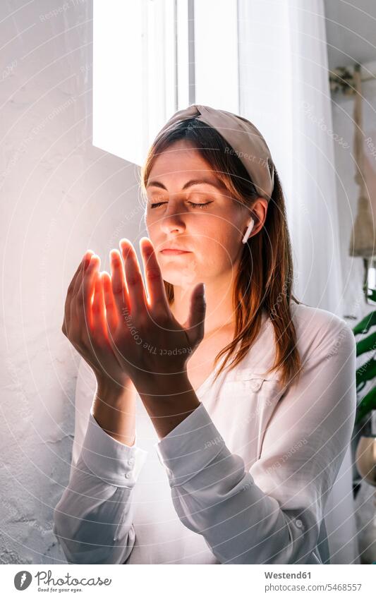 Beautiful woman praying with eyes closed by window at home color image colour image Spain indoors indoor shot indoor shots interior interior view Interiors day
