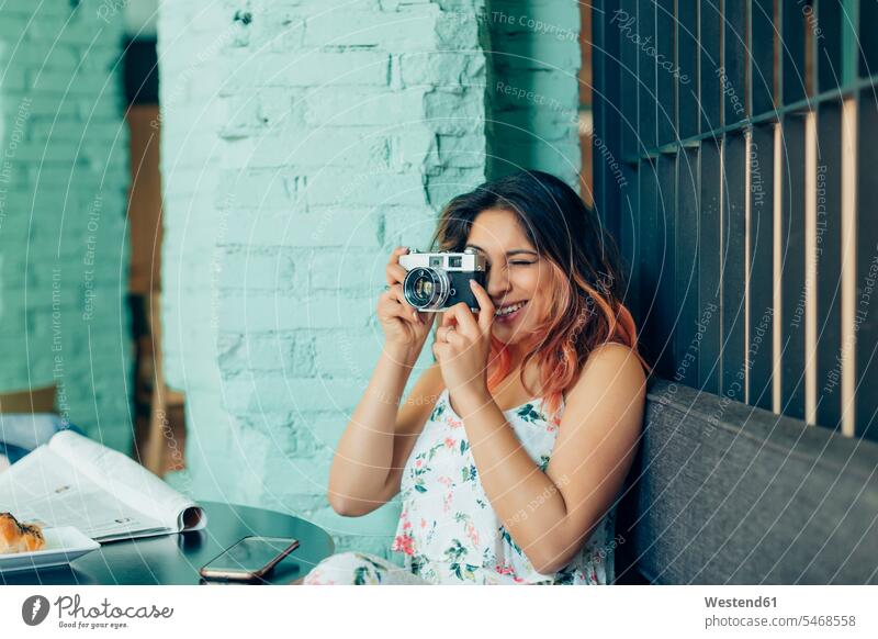 Smiling woman sitting in coffee shop taking pictures with camera Seated smiling smile cafe cameras females women Adults grown-ups grownups adult people persons