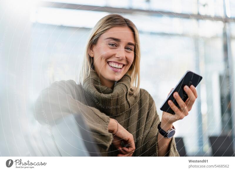Portrait of happy young woman sitting in waiting area with cell phone telecommunication phones telephone telephones cell phones Cellphone mobile mobile phones