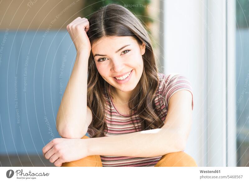 Portrait of smiling young woman sitting at the window at home Seated portrait portraits windows smile females women Adults grown-ups grownups adult people