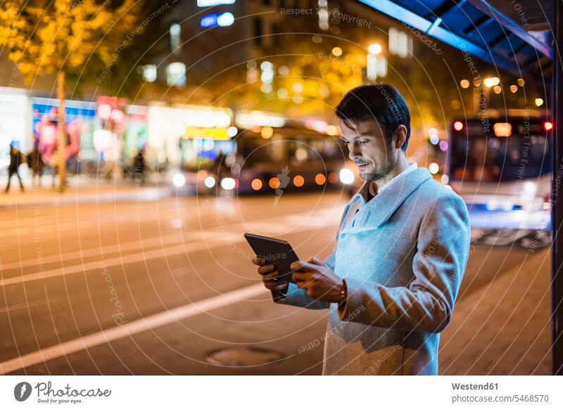 Businessman with digital tablet standing at a bus stop at night city town cities towns outdoors outdoor shots location shot location shots caucasian