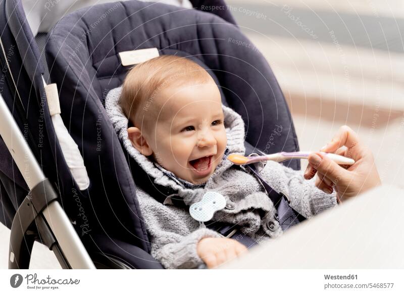 Mother feeding laughing baby boy in stroller Table Tables unrecognisable person Unrecognizable People Unrecognizable Person buggy one parent high spirits
