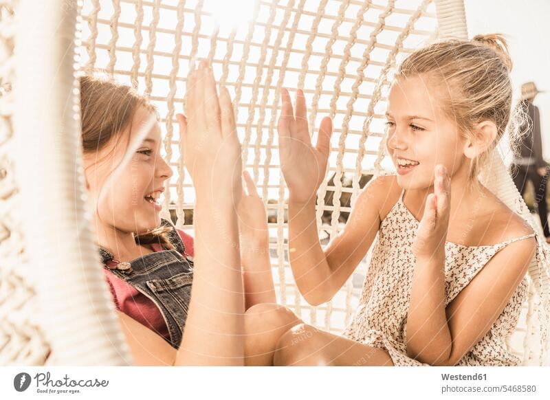 Two girls clapping hands in hanging chair friends mate female friend touristic tourists chairs clap hands Clapping smile Seated sit play seasons summer time