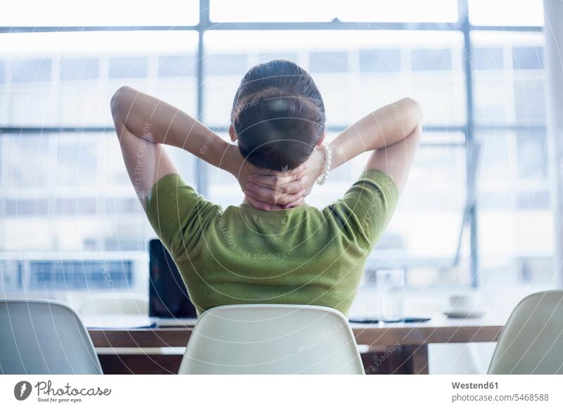 Tired businesswoman sitting with hands behind neck at desk in office color image colour image indoors indoor shot indoor shots interior interior view Interiors