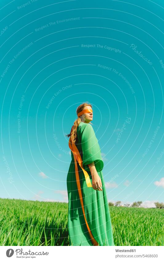 Blindfolded young woman wearing a green dress standing in a field band bands ribbons dresses relax relaxing seasons spring season Spring Time springtime