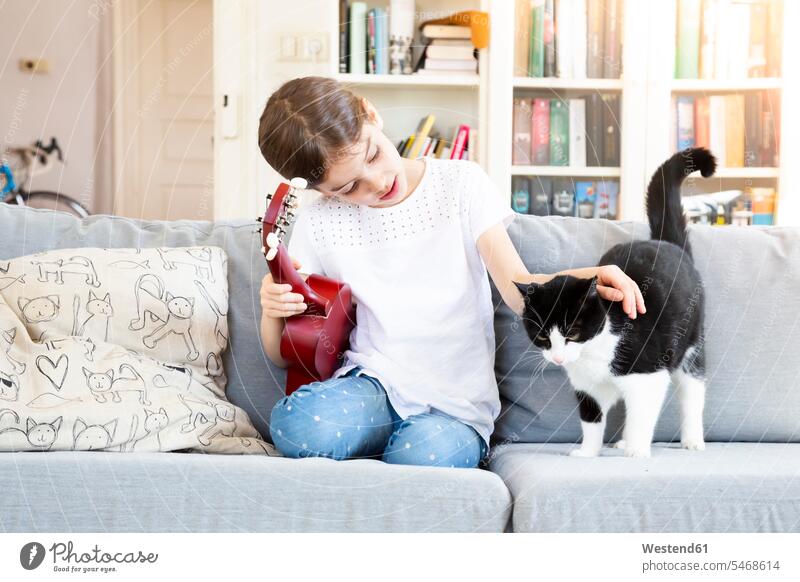 Girl with ukulele sitting on couch stroking cat cats Seated settee sofa sofas couches settees ukelele girl females girls pets animal creatures animals guitar