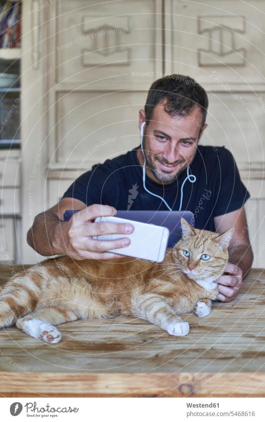 Man sitting at table, taking picture of his ginger cat with smartphone Occupation Work job jobs profession professional occupation photographers animals
