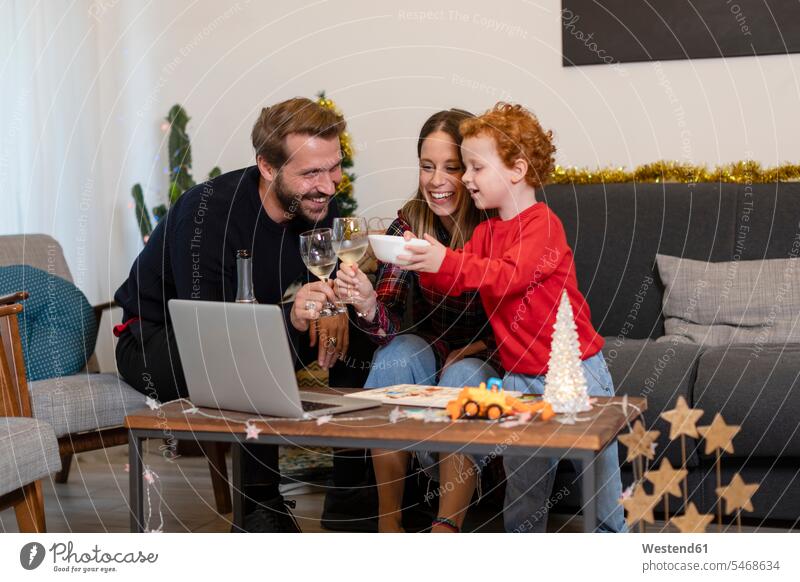 Happy family toasting drinks while video calling over laptop during Christmas celebration at home color image colour image casual clothing casual wear