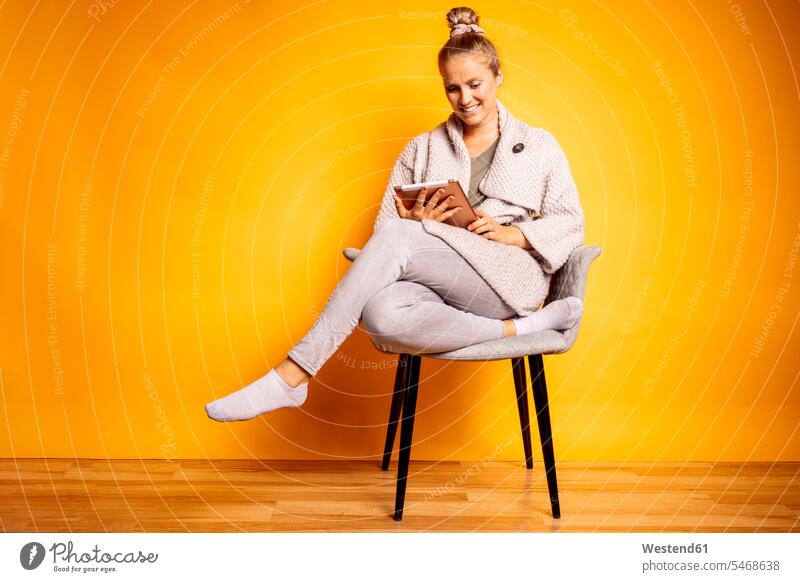 Smiling woman using digital tablet while sitting on chair against yellow background color image colour image coloured background colored background studio shot