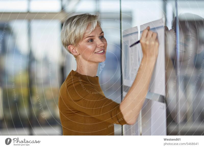 Smiling businesswoman writing on papers at glass pane glass panes confidence confident businesswomen business woman business women write smiling smile window