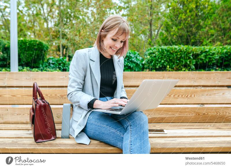 Smiling woman sitting on park bench using laptop Occupation Work job jobs profession professional occupation business life business world business person