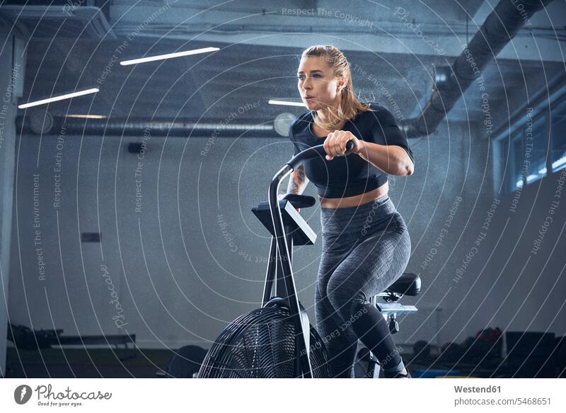 Athletic woman doing airbike workout at gym females women endurance gyms Health Club motion Movement moving bicycle bikes bicycles athlete sportswoman athletes