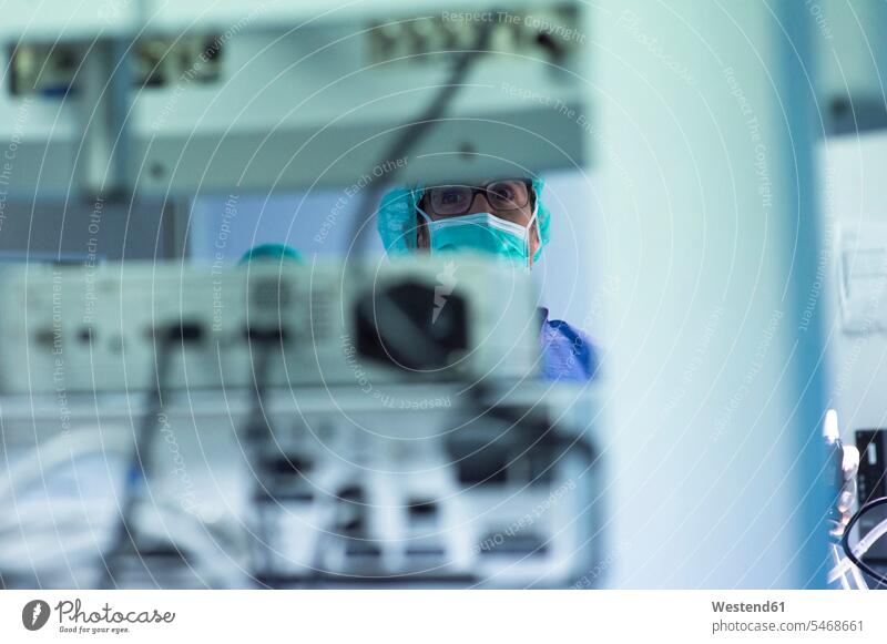 Focused male surgeon looking at monitoring equipment while operating in ICU color image colour image indoors indoor shot indoor shots interior interior view