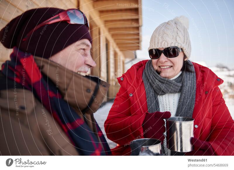 Happy mature couple with hot drinks outdoors at mountain hut in winter twosomes partnership couples happiness happy mountain shelter alpine hut mountain huts