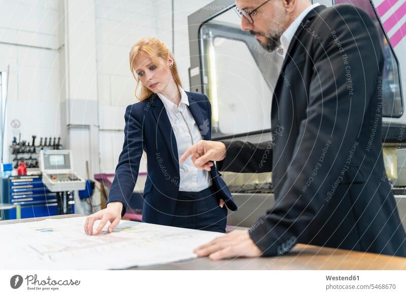 Businessman and businesswoman looking at plan on table in factory eyeing plans factories Business man Businessmen Business men businesswomen business woman