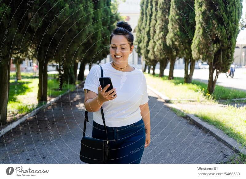 Smiling curvy young woman using mobile phone in a public park human human being human beings humans person persons adult grown-up grown-ups grownup grownups