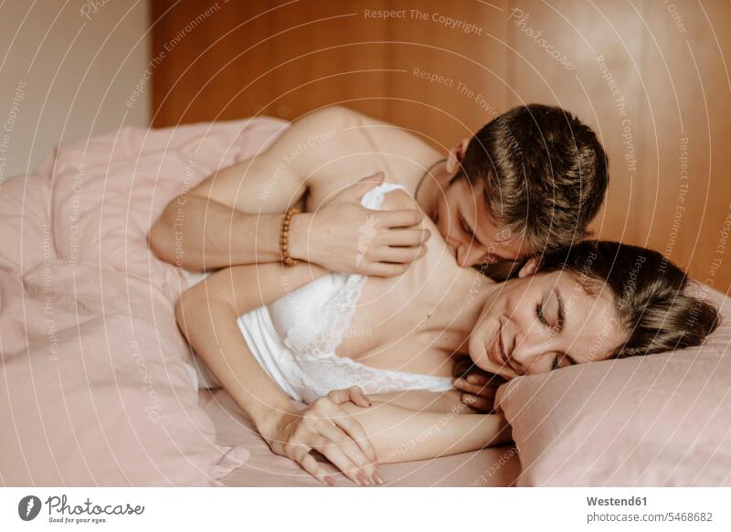 Intimate young couple lying in bed Bed - Furniture beds touch cuddle snuggle snuggling kiss kisses smile enjoy enjoyment indulgence indulging savoring happy