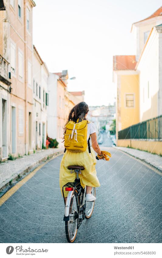 Woman with backpack riding bicycle on road amidst buildings in city color image colour image Portugal leisure activity leisure activities free time leisure time