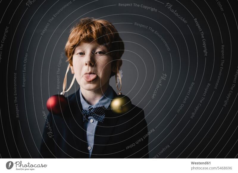 Portrait of redheaded boy wearing bow tie and Christmas baubles sticking out tongue human human being human beings humans person persons caucasian appearance