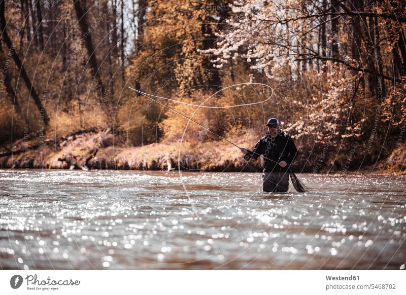 Fly Fisherman casting fishing line while standing in river at forest color image colour image outdoors location shots outdoor shot outdoor shots fisherman