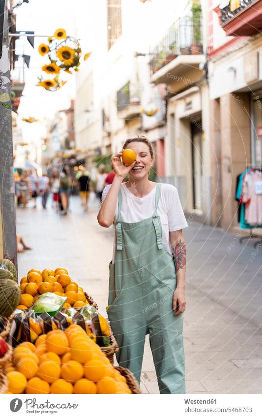 Portrait of laughing young woman on shopping street covering eye with an orange human human being human beings humans person persons caucasian appearance