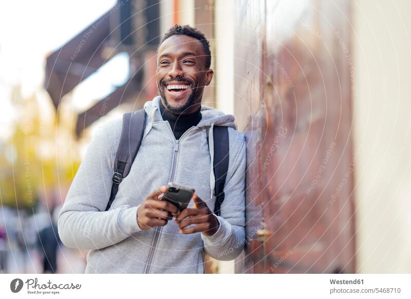 Smiling man using mobile phone while leaning on wall color image colour image outdoors location shots outdoor shot outdoor shots day daylight shot