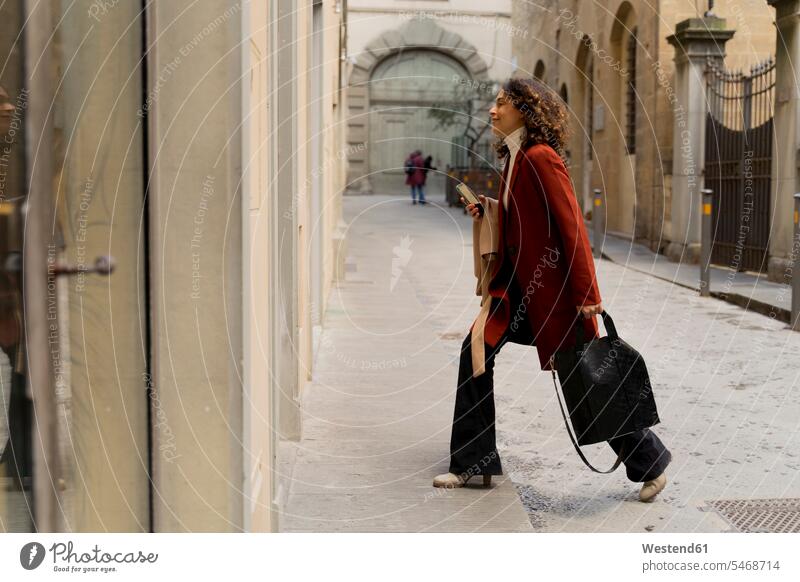Woman walking in an alley in the city, Florence, Italy human human being human beings humans person persons curl curled curls curly hair bags coat coats jackets