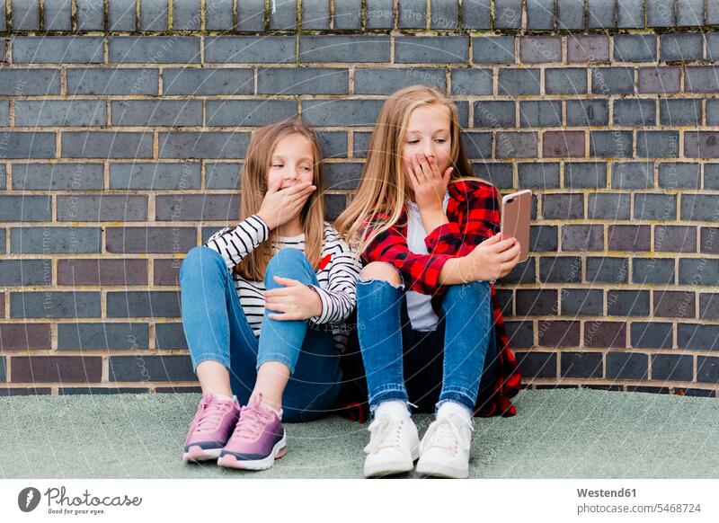 Portrait of two girls sitting in front of brick wall taking selfie with smartphone Smartphone iPhone Smartphones Selfie Selfies females brick walls Seated