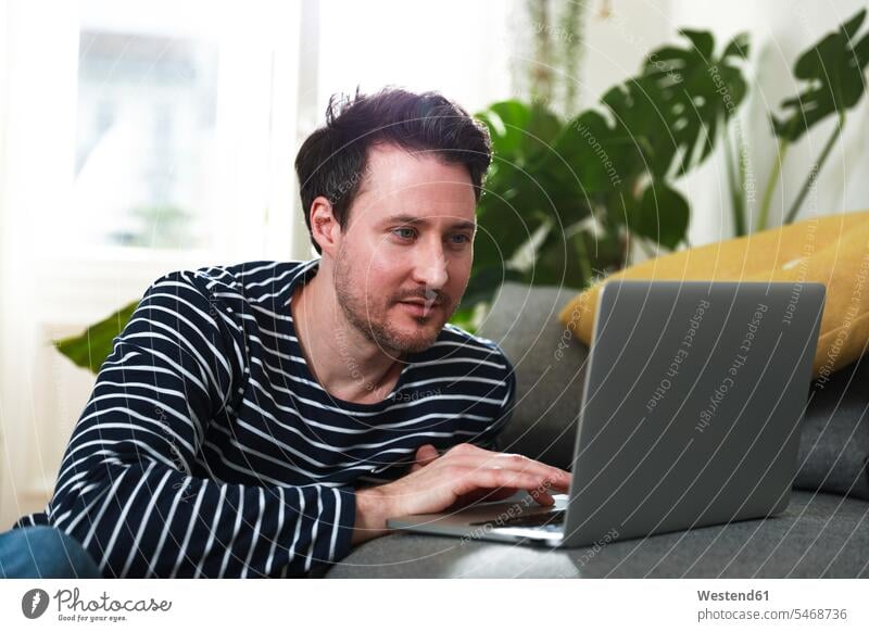 Man sitting at home, using laptop Seated using a laptop Using Laptops man men males Laptop Computers laptops notebook Adults grown-ups grownups adult people