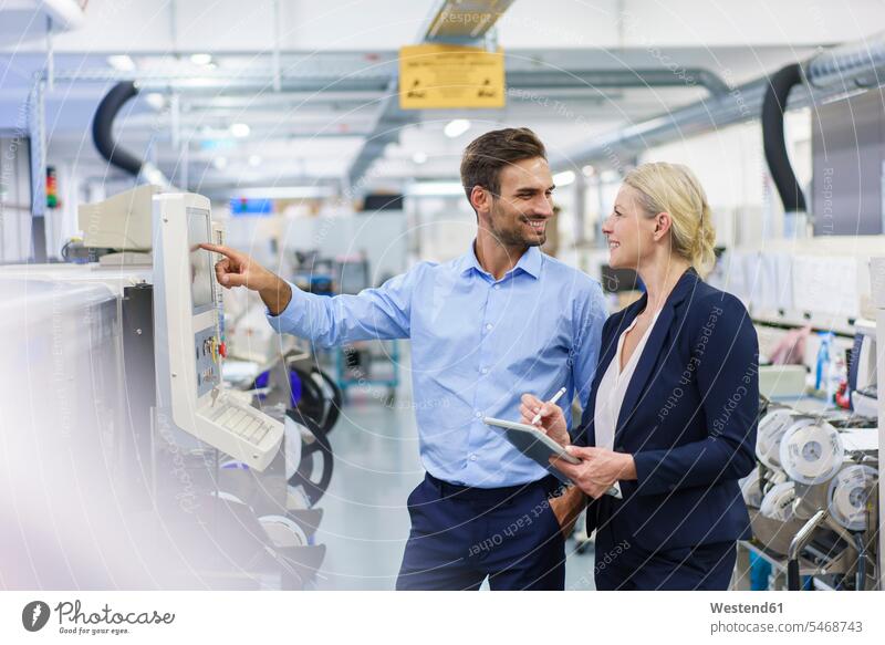 Smiling male technician looking at businesswoman while standing by machinery at illuminated factory color image colour image indoors indoor shot indoor shots