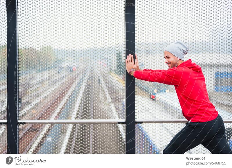 Young man stretching on a railway bridge exercise practising train training hear smile exercising practice practise delight enjoyment Pleasant pleasure colour
