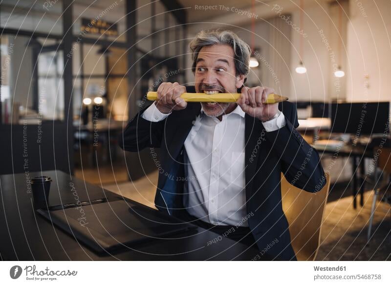Angry senior businessman with giant pencil at desk in office Occupation Work job jobs profession professional occupation business life business world