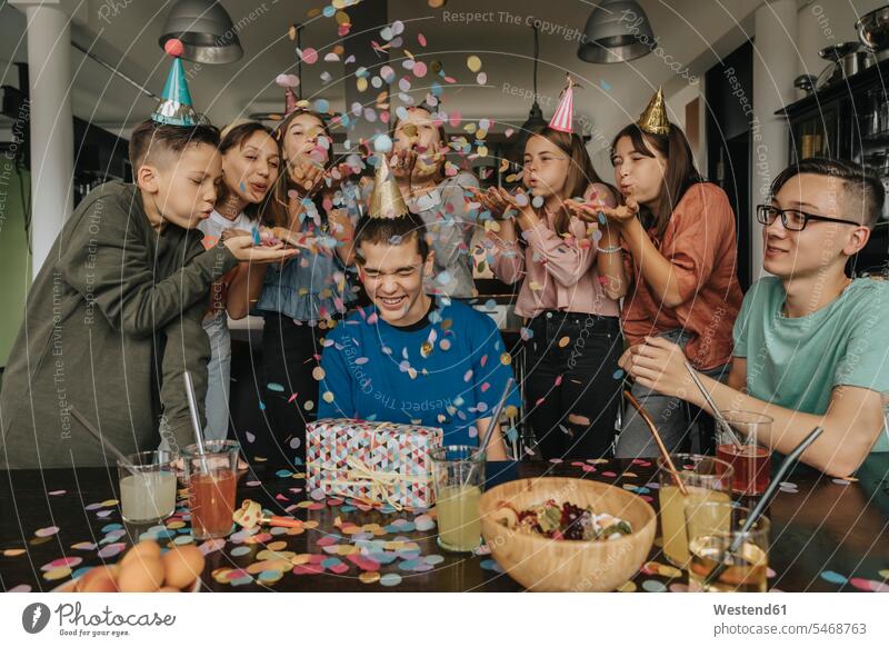 Friends throwing confetti on birthday boy sitting with gift at dining table color image colour image Germany indoors indoor shot indoor shots interior