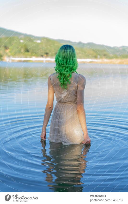 Back view of young woman with dyed green hair standing dressed in water of lake females women coloured lakes people persons human being humans human beings