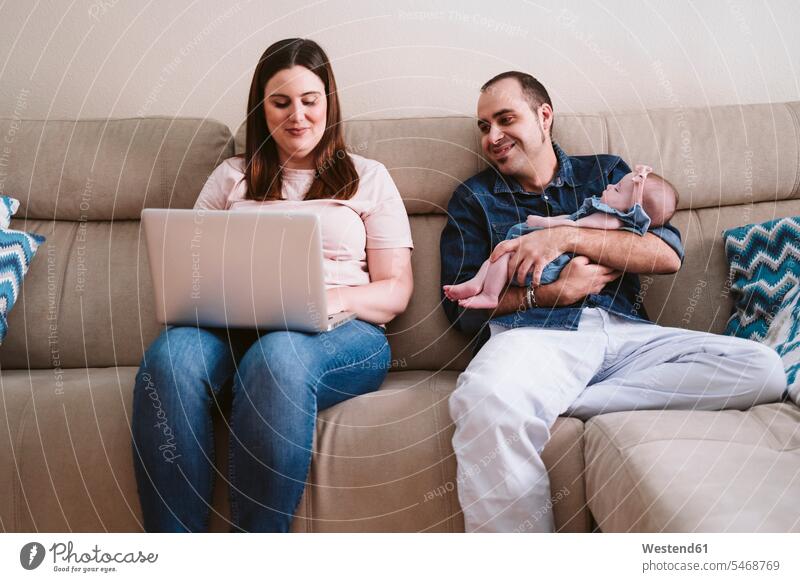 Father carrying sleeping daughter while looking at woman using laptop on sofa color image colour image indoors indoor shot indoor shots interior interior view