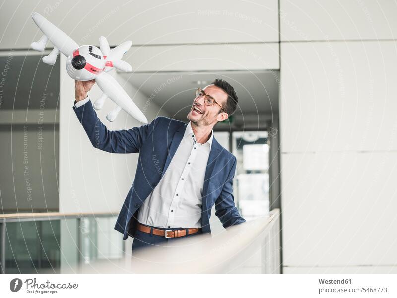 Laughing businessman playing with toy aeroplane in office building offices office room office rooms airplane aeroplanes airplanes toys air travel air travelling
