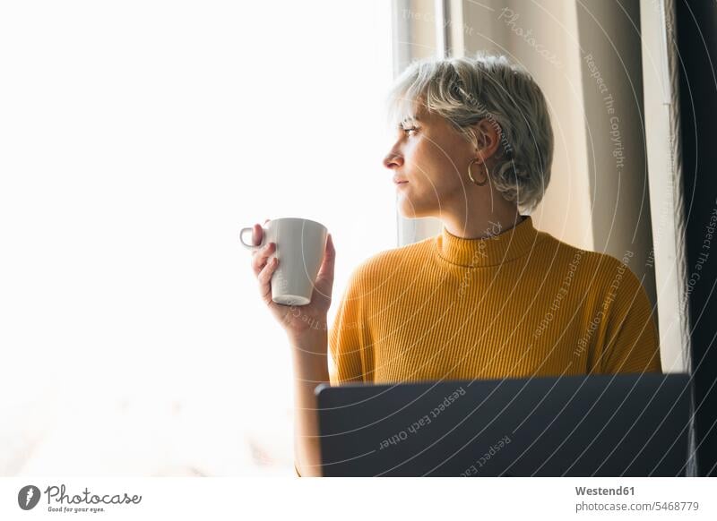 Woman looking out of window at home with laptop and coffee cup human human being human beings humans person persons celibate celibates singles solitary people