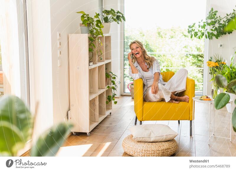 Portrait of laughing mature woman on the phne relaxing in armchair at home cushions rack racks Shelve shelves telecommunication phones telephone telephones