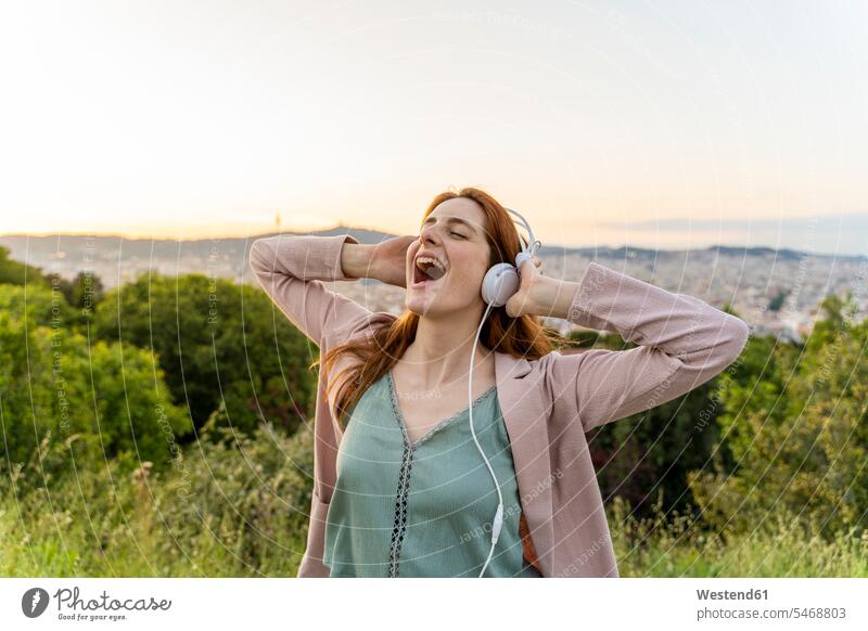 Young redheaded woman with headphones on view point headset hear cheer exultation jubilate jubilating rejoice rejoicing smile sing in the evening Ardor Ardour