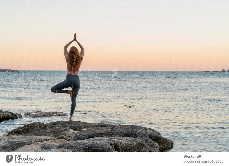 Young woman practicing yoga on the beach, doing tree pose, during sunset in calm beach, Costa Brava, Spain human human being human beings humans person persons