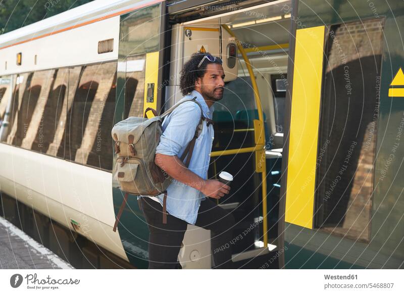 Young trendy man boarding train at railroad station color image colour image outdoors location shots outdoor shot outdoor shots day daylight shot daylight shots