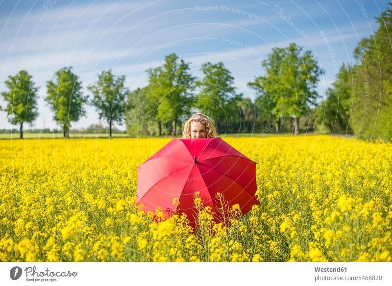 Mature woman with red umbrella standing amidst oilseed rapes against sky color image colour image Germany leisure activity leisure activities free time